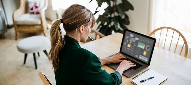 a worker reviews a dashboard of data on a laptop at the kitchen table in a home
